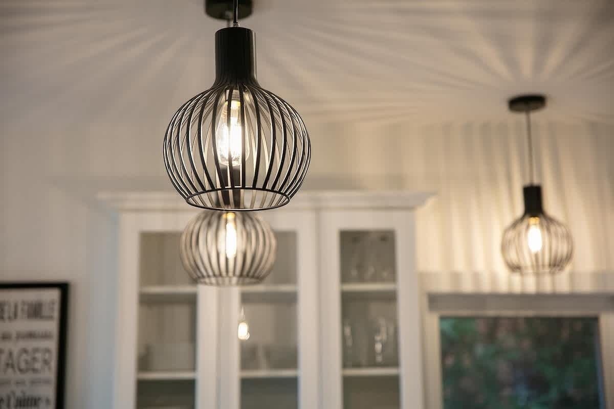 A room with two pendant lights hanging from the ceiling, a white cabinet with glass doors, and a framed sign on the wall.