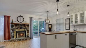 A modern kitchen with a stone fireplace, wooden cabinets, and a large window.