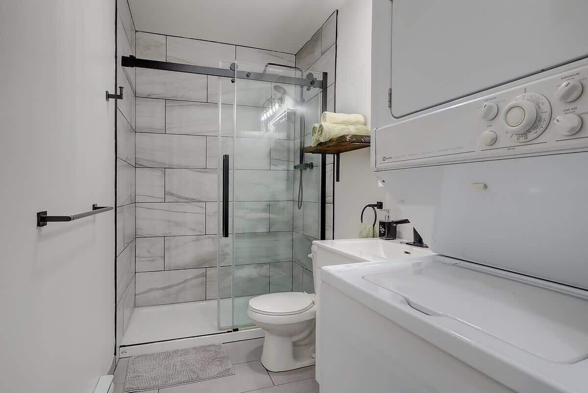 Un baño moderno con ducha envuelta en vidrio, inodoro y lavamanos blancos.