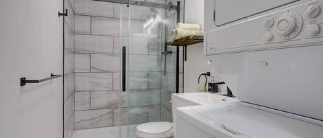 Un baño moderno con ducha envuelta en vidrio, inodoro y lavamanos blancos.