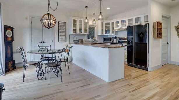 A modern kitchen with white cabinets, a central island, pendant lighting, and a vintage clock.