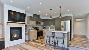 Une cuisine moderne avec une cheminée, des meubles en bois, un grand téléviseur et un coin bar avec des tabourets.