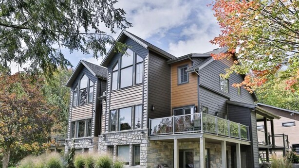 Une maison moderne à deux étages, dotée d’une façade en pierre, de grandes fenêtres et d’un balcon.