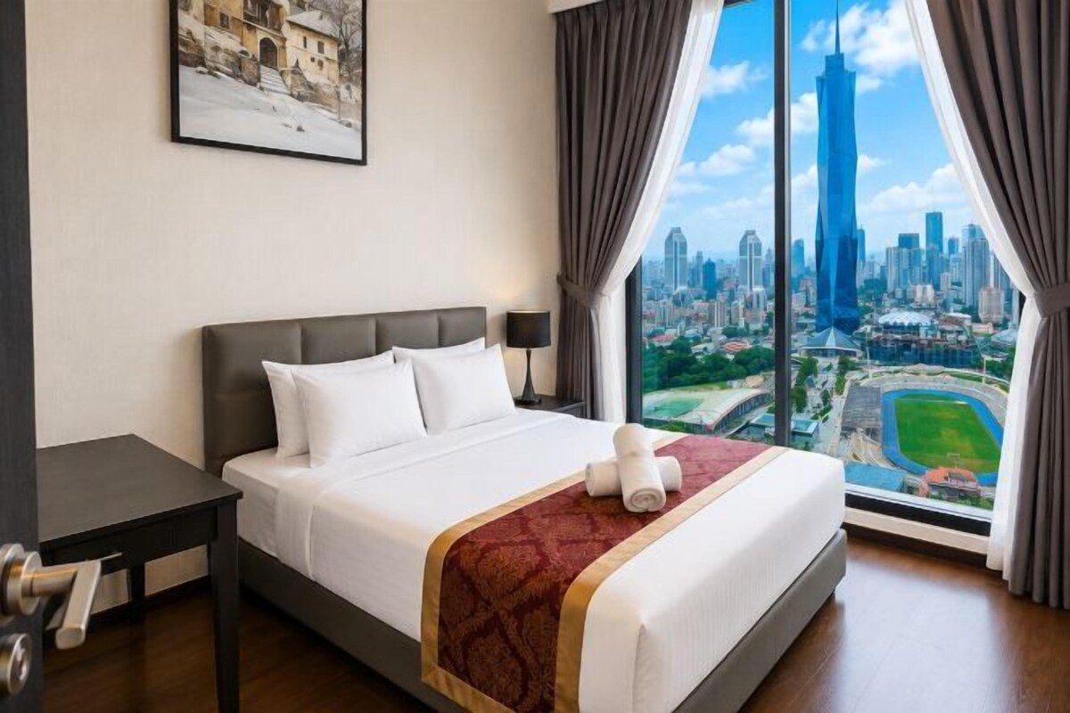 A hotel room with a large bed, a nightstand, a window with a city view, and a framed picture on the wall.
