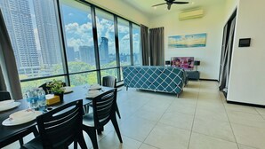 A modern living room with a dining area, large windows with a city view, a ceiling fan, and a flat-screen TV. - Opus Residences Merdeka Tower KL (Kuala Lumpur)