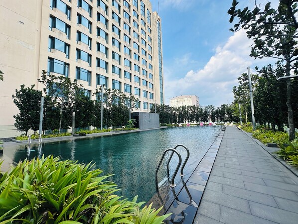Un edificio moderno con piscina y un paseo bordeado de árboles.