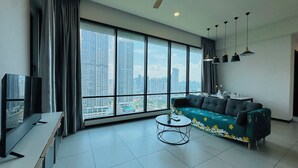 A modern living room with a large window, a sofa, a coffee table, and a TV. - Opus Residences Merdeka Tower KL (Kuala Lumpur)