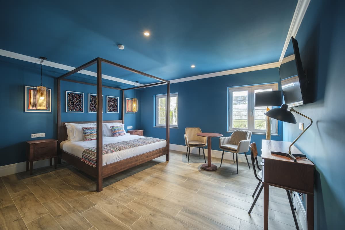 Een slaapkamer met een hemelbed, een bureau met een stoel, en een televisie aan de muur.