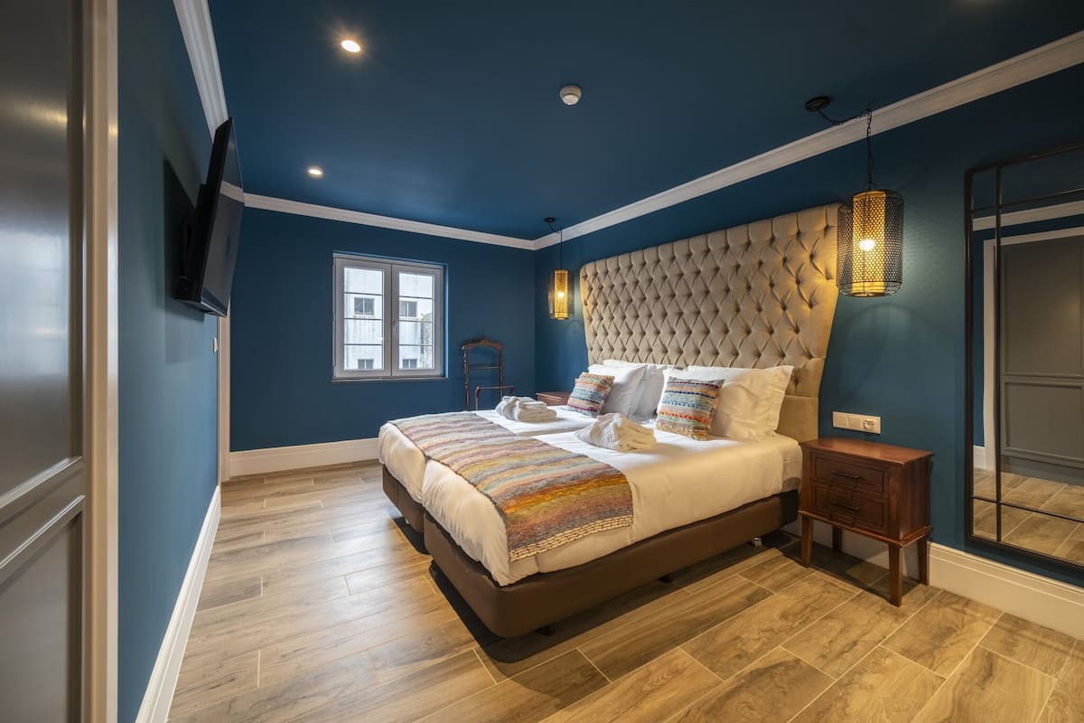 Een slaapkamer met een groot bed, een raam, een tv aan de muur en een nachtkastje.