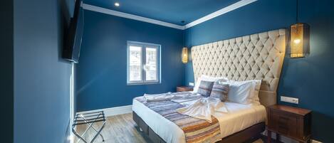 A bedroom with a large bed, a TV mounted on the wall, a window, and a hanging light fixture.