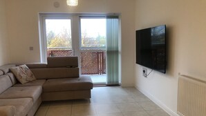 Una sala de estar con un sofá seccional color beige, un televisor de pantalla plana montado en la pared y una puerta corrediza de vidrio que da a un área exterior.