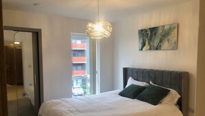 Un dormitorio con cama, lámpara colgante, un cuadro en la pared y vista a un edificio.