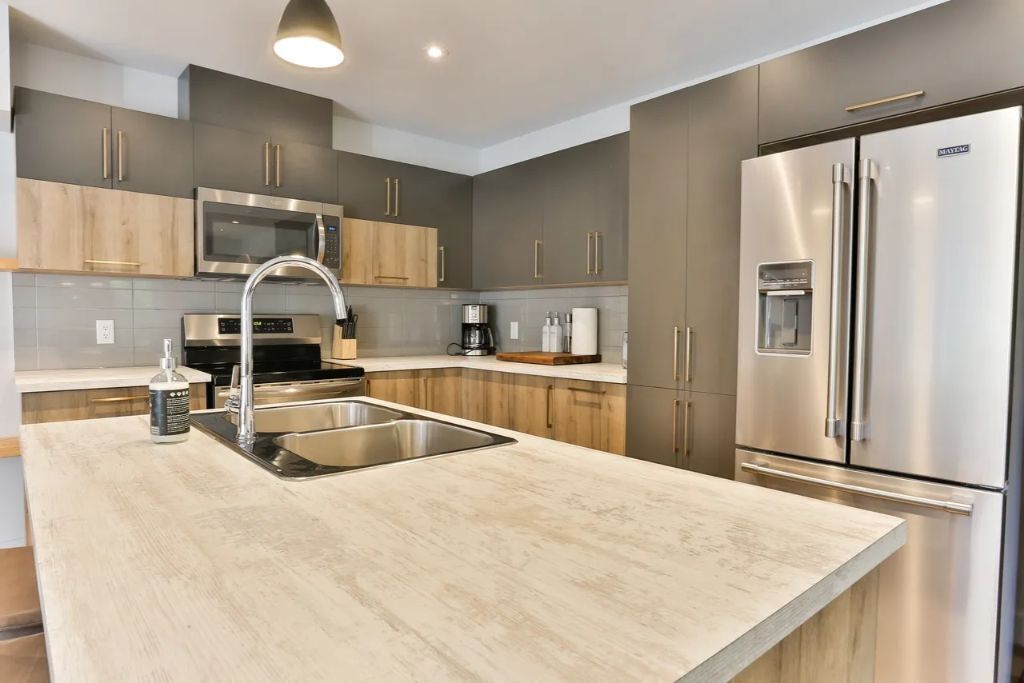 A modern kitchen with grey cabinets, stainless steel appliances, a double sink, and a built-in oven.