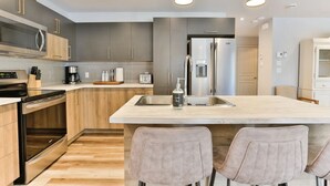 Une cuisine moderne dotée d’un îlot central, d’appareils électroménagers en acier inoxydable et de luminaires suspendus.