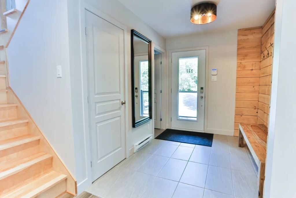 Un couloir propre et moderne, avec des murs blancs, un escalier en bois et un lambris en bois sur le côté droit.