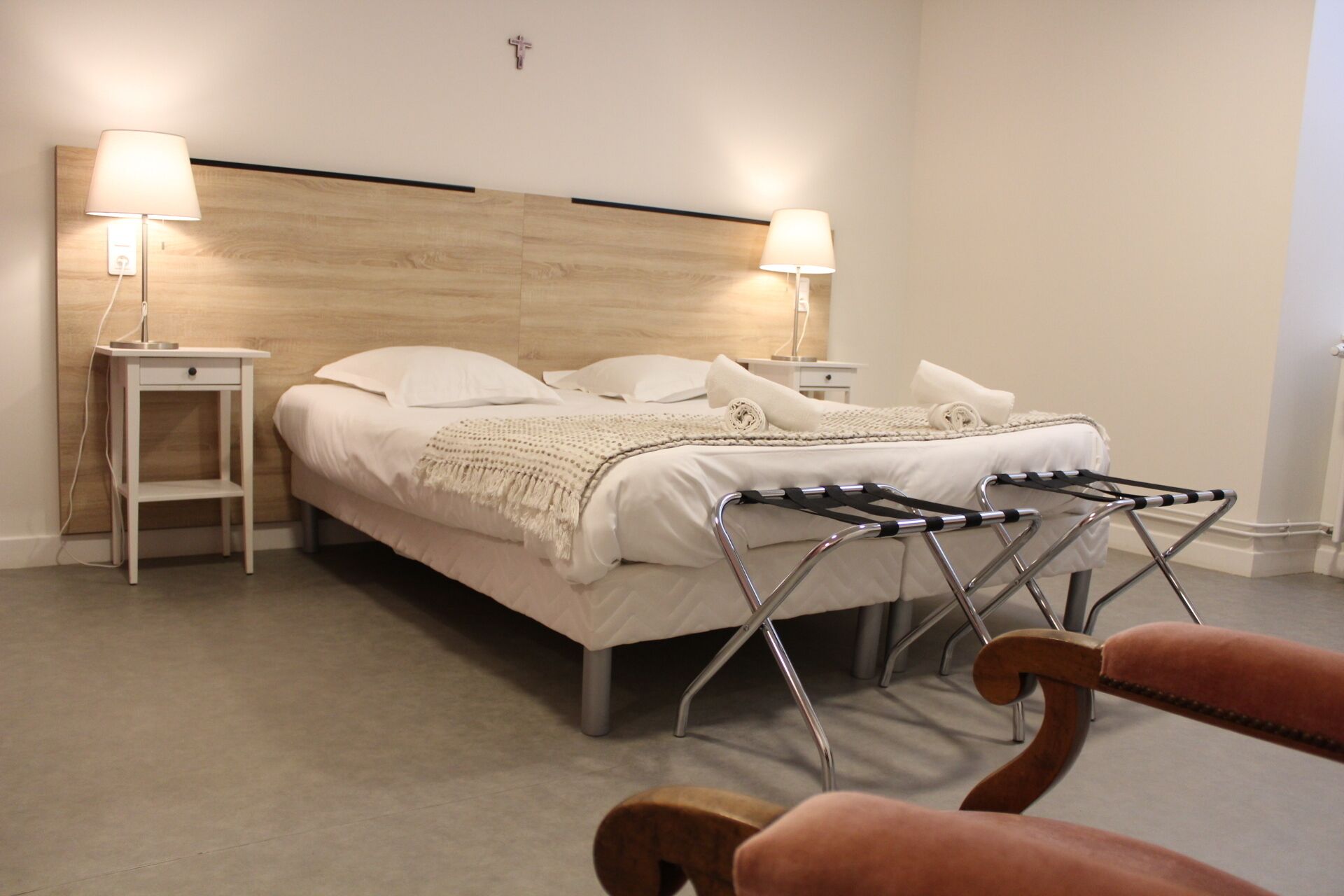 Cama bem arrumada com cabeceira de madeira, duas mesas de cabeceira com abajures e um varal de metal.