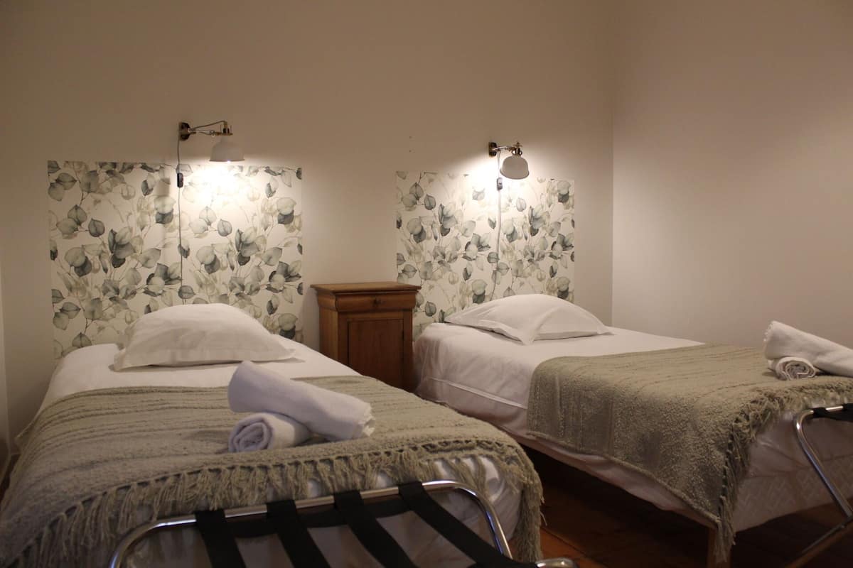Une chambre d’hôtel avec deux lits, chacun doté d’une tête de lit, d’une table de chevet en bois et d’une lampe fixée au mur.