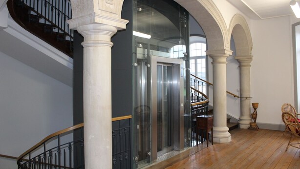 A spacious interior with a staircase, a glass elevator, and classical architecture. - Le Grand Couvent de Gramat (Gramat)
