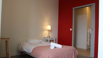 A bedroom with a bed, a bedside table with a lamp, a red wall, and a door leading to a bathroom.