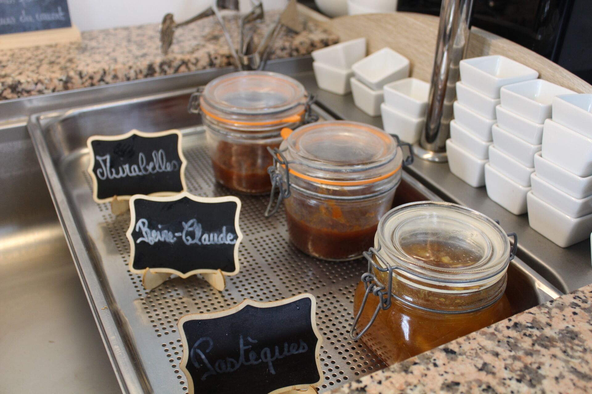 A kitchen counter with three glass jars labeled 'Thé', 'Raisin-Clande', and 'Lactées'.