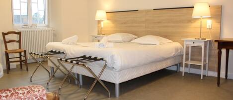 Habitación de hotel con una cama, dos lámparas de noche, un cabecero de madera, un radiador, una silla y una mesita.
