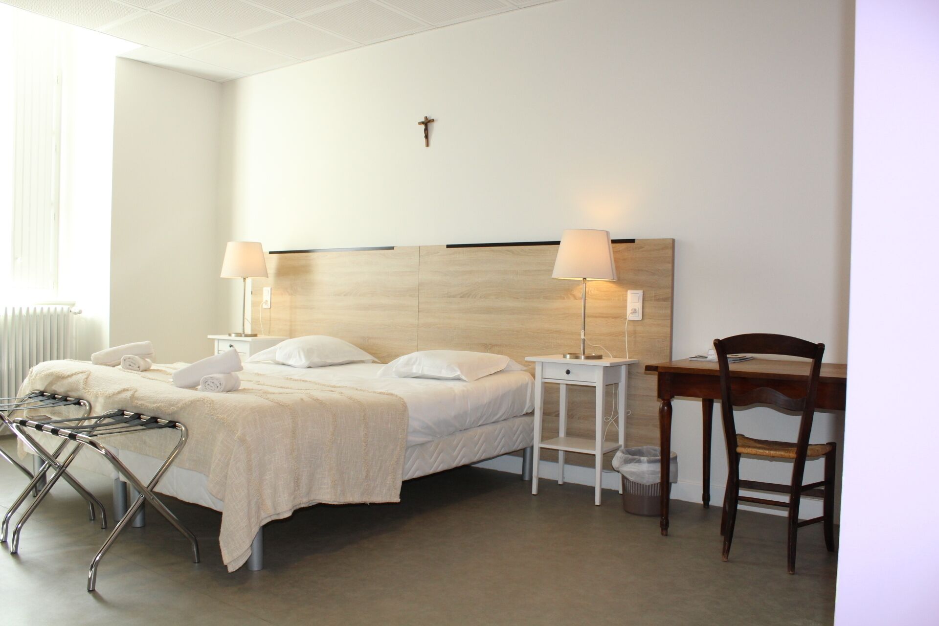 Una camera d'hotel con un letto, abat-jour, una testiera in legno, una scrivania e una sedia.