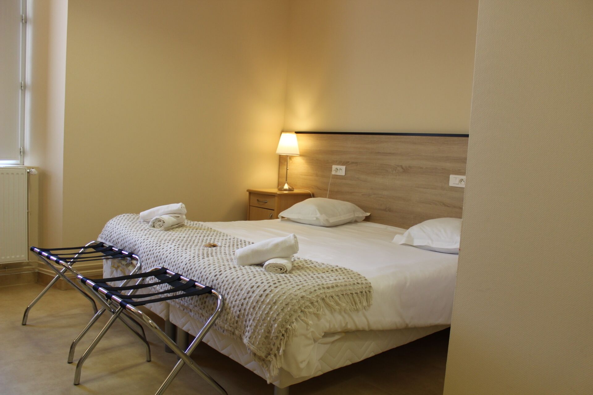 A hotel room with a bed, a nightstand, a lamp, and a drying rack.