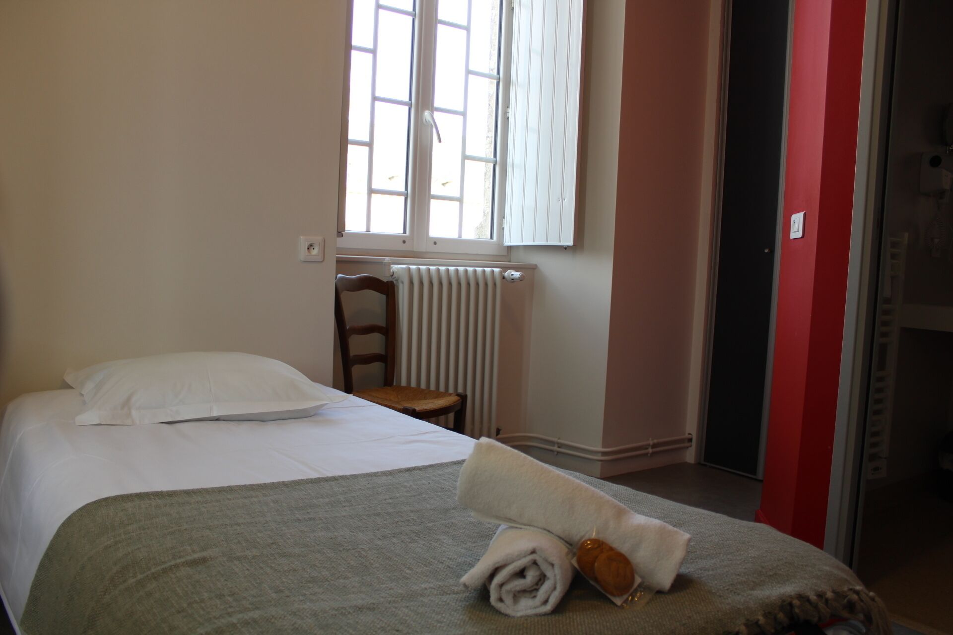 Un dormitorio con una cama, una silla, un radiador y una ventana.