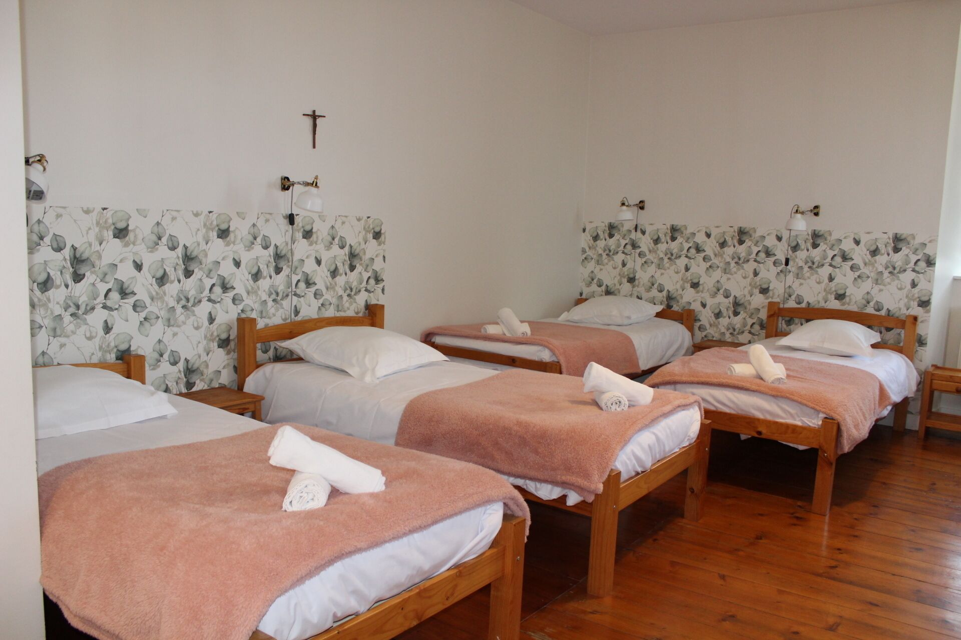A room with four wooden beds, each with a pink towel and white linens.