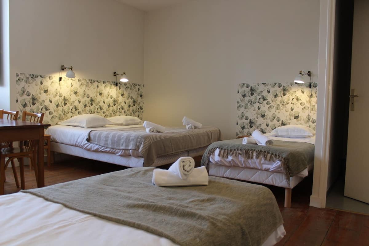 Une chambre d’hôtel avec deux lits simples, une table en bois et un grand lit au premier plan.