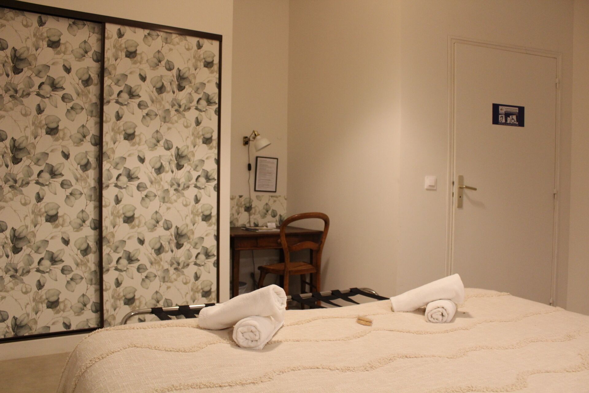 A hotel room with a bed, a chair, a desk, and a door.