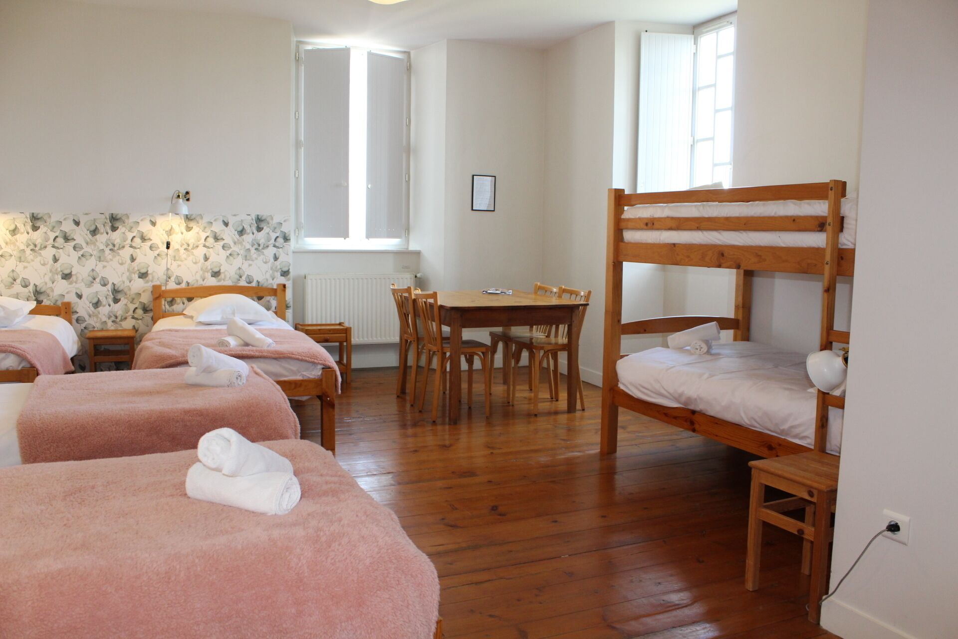 A room with two wooden bunk beds, a wooden table with chairs, and two single beds with pink towels.
