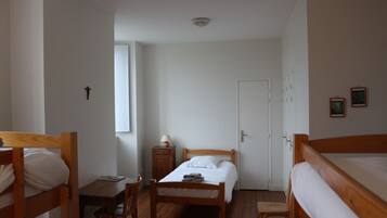 Un dormitorio con dos literas de madera, una cama individual, una mesita con lámpara, un armario y una puerta.