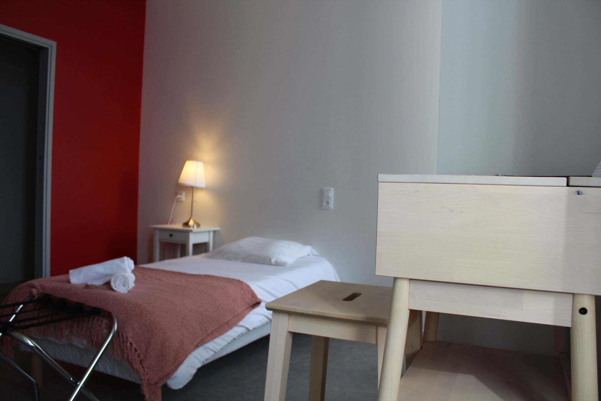 Une chambre d’hôtel comprenant un lit, une table de chevet avec une lampe, un petit bureau et une chaise.