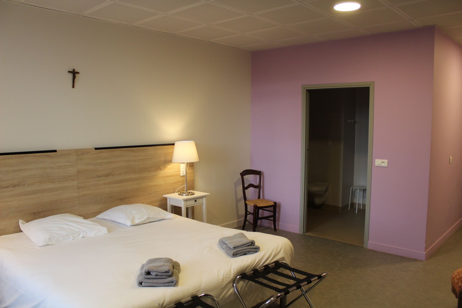 Une chambre d’hôtel avec un lit, une chaise, une table de chevet et une lampe.