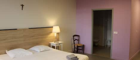 Habitación de hotel con cama, una silla, mesita de noche y lámpara.