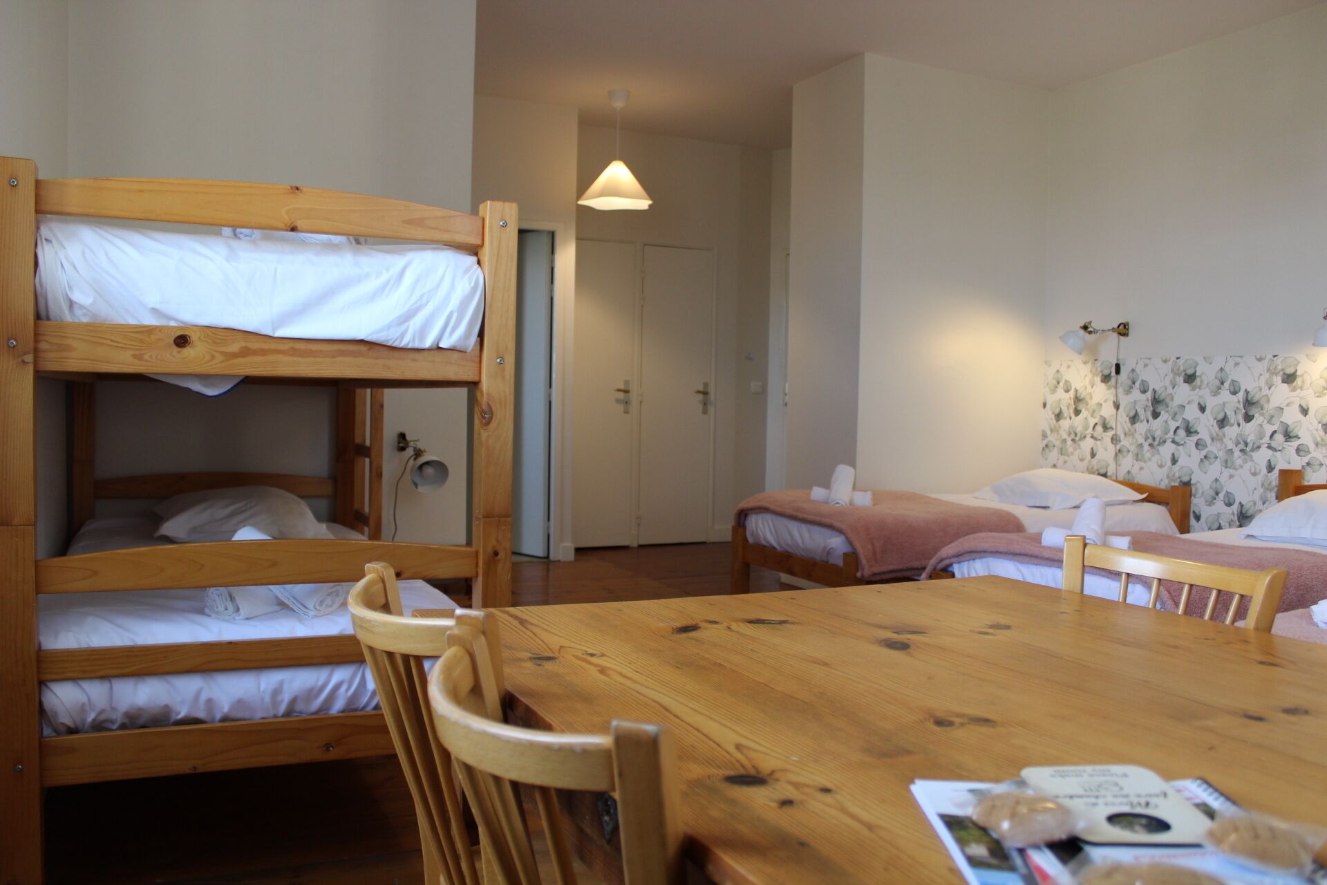 Une chambre avec des lits superposés, une table en bois et un lit séparé avec un papier peint à motifs floraux.