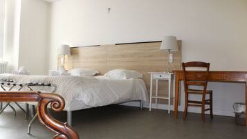 A hotel room with a bed, bedside lamps, a wooden chair, a desk, and a cross on the wall.