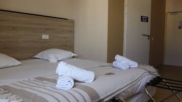 Een hotelkamer met een houten hoofdeinde, twee witte kussens, een gestreept dekbed en opgerolde handdoeken op het bed.