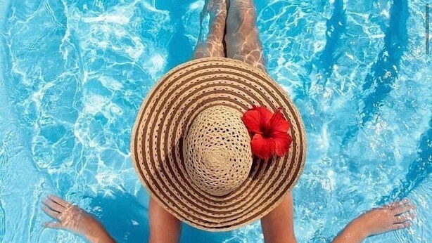 Una persona sdraiata su una poltrona a bordo piscina, con la schiena rivolta alla fotocamera, e una vista libera sull'acqua della piscina.