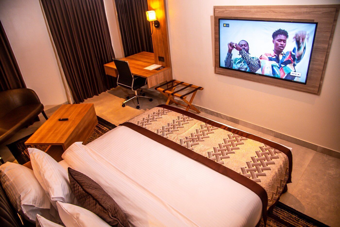 A hotel room with a bed, a desk, a chair, and a TV on the wall.