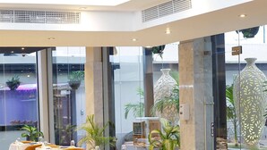 Una hall moderna di un hotel con un’area salotto a forma di curva, ampie finestre e piante in vaso.