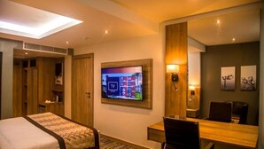 Una camera d'albergo con un letto, una scrivania con una sedia, un televisore fissato al muro e un grande specchio.