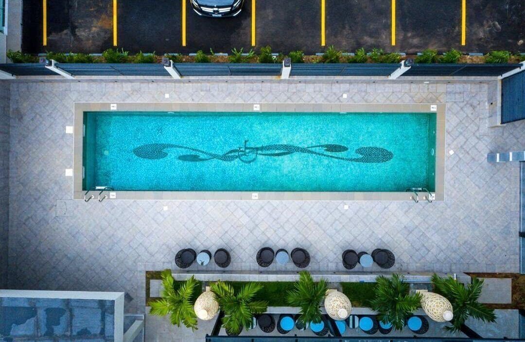 A rectangular swimming pool with a decorative design, surrounded by a tiled patio with seating and plants.