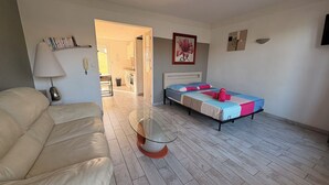 Une chambre avec un lit, un canapé, une table en verre et, au fond, un coin cuisine.