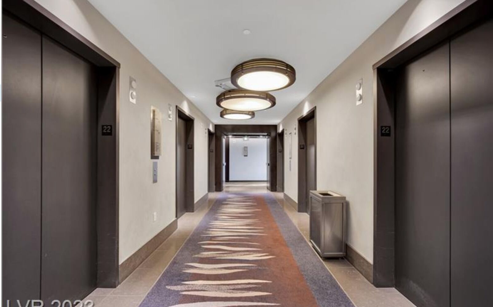 A modern hallway with dark elevators, a patterned carpet, and a trash bin.
