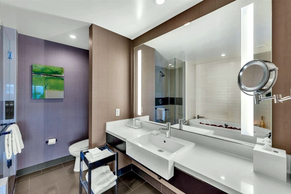A modern bathroom with a large mirror, two sinks, and a shower area.