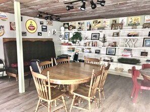 A dining area with a round wooden table and six chairs, surrounded by shelves with various items and memorabilia. - Old Rustic Country store near Pine mtn. / Kingdom Come Park & Bad Branch Falls  (Partridge)
