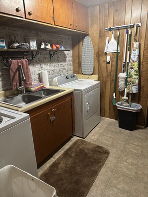 A compact kitchen with wooden cabinets, a washing machine, a sink, and a drying rack. - Old Rustic Country store near Pine mtn. / Kingdom Come Park & Bad Branch Falls  (Partridge)