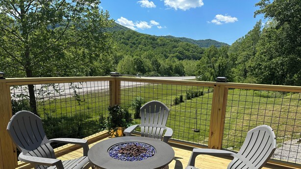 Una terraza con una mesa y sillas alrededor de una chimenea, con vistas a un área verde y montañas.